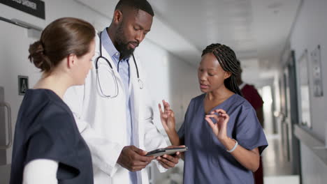 Diverse-male-and-female-doctors-discussing-work,-using-tablet-in-corridor-at-hospital,-slow-motion