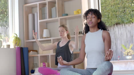 Focused-diverse-fitness-women-exercising-and-meditating-on-mat-in-white-room,-slow-motion