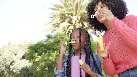 Happy-african-american-mother-with-daughter-blowing-bubbles-in-garden-at-home,-slow-motion