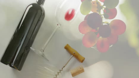 Composite-of-red-wine-bottle-and-glass-with-corcscrew-over-grapes-background