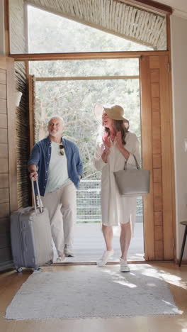 Vertical-video-of-happy-senior-caucasian-couple-walking-through-door-with-suitcase,-slow-motion