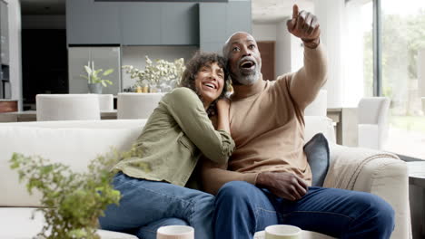 Happy-biracial-couple-embracing-and-watching-tv-at-home,-slow-motion