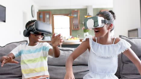 Happy-african-american-brother-and-sister-using-vr-headsets-on-sofa,-slow-motion