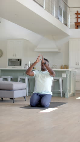 Hombre-Afroamericano-Enfocado-Practicando-Meditación-De-Yoga-En-Una-Sala-De-Estar-Soleada,-Cámara-Lenta