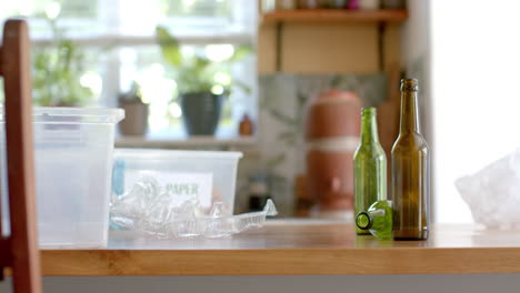 Segregation-plastic-boxes-for-waste,-plastic-and-glass-bottles-on-table-in-kitchen,-slow-motion