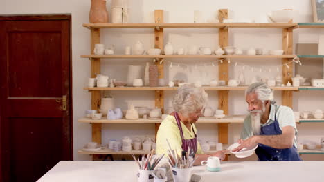 Happy-biracial-male-and-female-potters-with-plate,-discussing-in-pottery-studio,-slow-motion
