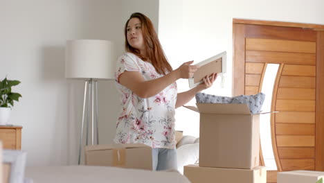 Happy-plus-size-biracial-woman-unpacking-picture-from-box-in-new-home,-slow-motion