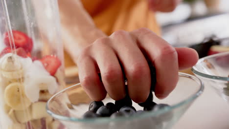 Hand-of-biracial-man-making-smoothie-putting-chopping-fruit-in-blender,-copy-space,-slow-motion