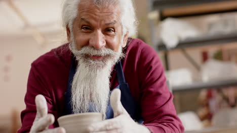 Happy-senior-biracial-potter-working-on-clay-vase-and-smiling-in-pottery-studio,-slow-motion