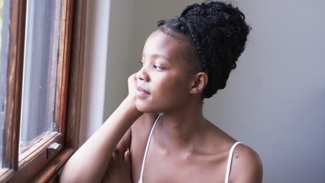 Young-African-American-woman-gazes-out-a-window,-with-copy-space