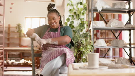 Happy-african-american-female-potter-sitting-and-smiling-in-pottery-studio,-slow-motion