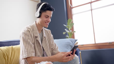Happy-biracial-man-wearing-headphones-having-video-call-on-smartphone,-copy-space,-slow-motion