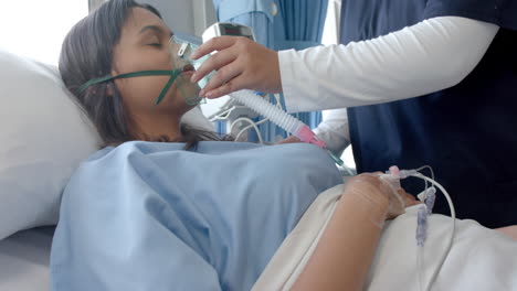 Diverse-female-patient-in-hospital-bed-and-female-doctor-putting-oxygen-mask-on-her,-slow-motion