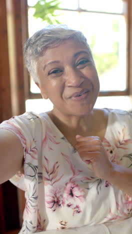 Video-Vertical-De-Retrato-De-Una-Feliz-Mujer-Birracial-Mayor-Teniendo-Videollamada-En-Casa,-Cámara-Lenta