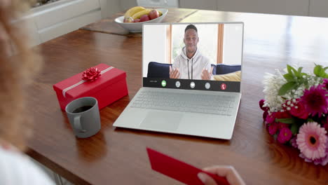 Caucasian-woman-holding-red-envelope-using-laptop-with-african-american-man-on-screen