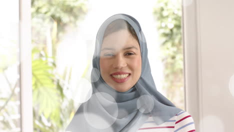 Animation-of-leaves-over-biracial-woman-in-hijab-smiling