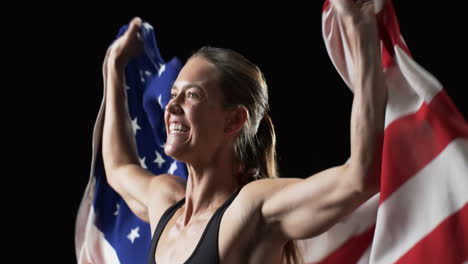 Patriotic-young-Caucasian-woman-athlete-holds-the-American-flag-with-pride-on-a-black-background