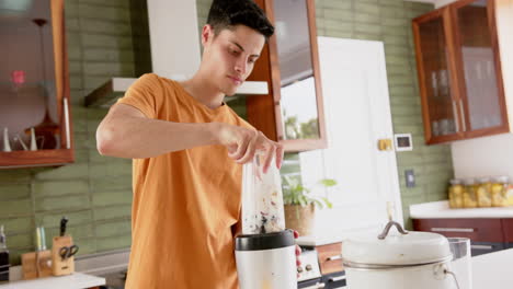 Focused-biracial-man-preparing-fruit-smoothie-with-blender-in-kitchen,-copy-space,-slow-motion