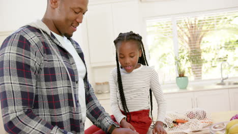 Glückliche-Afroamerikanische-Eltern-Und-Tochter-Packen-Zu-Hause-Ihre-Einkaufstasche-Aus,-Zeitlupe