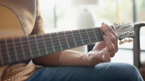 Midsection-of-senior-biracial-man-playing-guitar-in-sunny-room-at-home,-slow-motion
