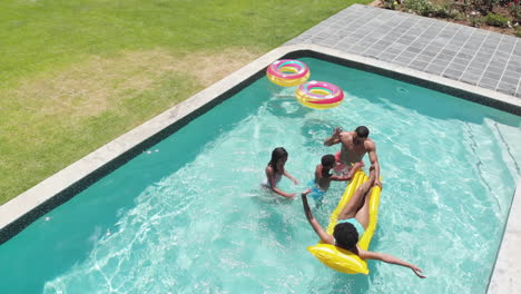 Happy-african-american-son-and-daughter-jumping-into-swimming-pool-to-parents