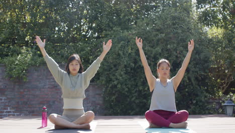 Focused-asian-female-friends-practicing-yoga-meditation-on-sunny-terrace,-slow-motion