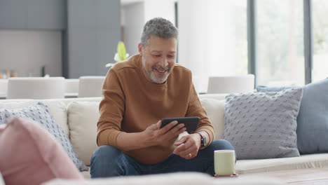 Glücklicher-älterer-Mann-Mit-Gemischter-Abstammung,-Der-Auf-Der-Couch-Im-Sonnigen-Wohnzimmer-Einen-Smartphone-Videoanruf-Führt,-Zeitlupe