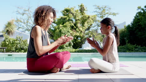 Happy-biracial-mother-and-daughter-practicing-yoga-sitting-in-sunny-garden,-slow-motion