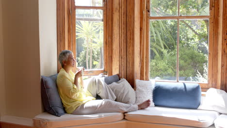 Glückliche-ältere-Frau-Mit-Gemischter-Abstammung,-Die-Auf-Der-Couch-Sitzt-Und-Zu-Hause-Tee-Trinkt,-Zeitlupe