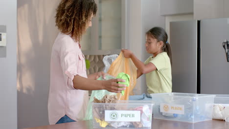 Happy-biracial-mother-and-daughter-sorting-rubbish-for-recycling-in-kitchen,-slow-motion