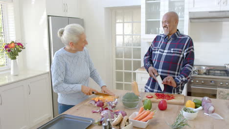 Happy-diverse-senior-couple-talking-and-cutting-vegetables-in-kitchen,-slow-motion