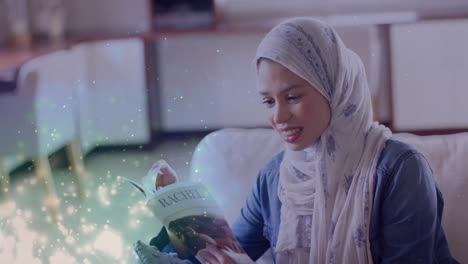 Animation-of-leaves-over-biracial-woman-in-hijab-smiling-and-reading-book