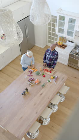 Video-Vertical-De-Una-Feliz-Pareja-Birracial-Mayor-Cocinando-Y-Cortando-Verduras,-Cámara-Lenta