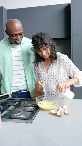 Happy-diverse-mature-couple-embracing-and-preparing-eggs-in-kitchen-at-home,-copy-space,-slow-motion