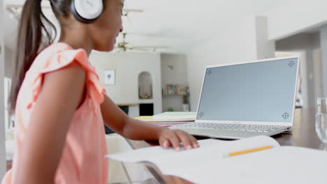 Happy-biracial-girl-in-headphones-having-school-class-on-laptop,-copy-space-on-screen,-slow-motion