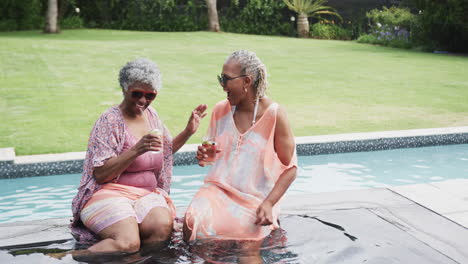 Happy-senior-african-american-female-friends-with-drinks-talking-by-pool,-copy-space,-slow-motion