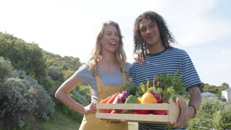 Portrait-of-happy-diverse-couple-holding-basket-of-fresh-vegetables-in-garden,-slow-motion