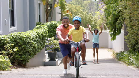 African-american-father-teaching-son-to-ride-bicycle,-mother-and-sister-cheering,-slow-motion