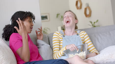 Happy-diverse-teenage-female-friends-talking-and-eating-popcorn-on-couch-at-home,-slow-motion