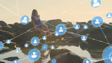 Animation-of-network-of-connected-icons-in-circles-over-happy-caucasian-woman-on-beach