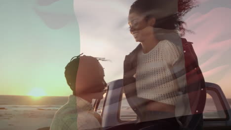 Animation-Der-Italienischen-Flagge-über-Einem-Glücklichen,-Vielfältigen-Paar,-Das-Sich-Mit-Dem-Auto-Am-Strand-Bei-Sonnenuntergang-Umarmt