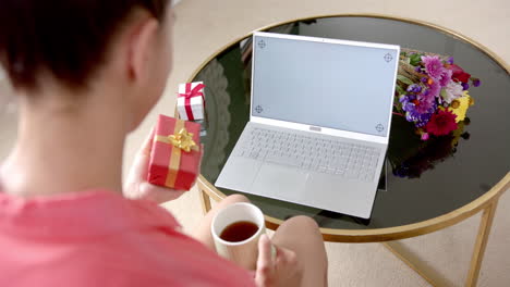 Biracial-teenage-girl-holding-gift-having-laptop-video-call-with-copy-space-screen,-slow-motion