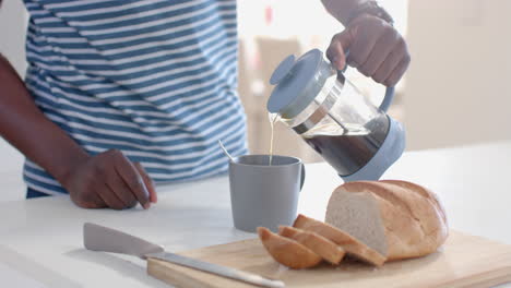 Afroamerikanischer-Mann-Gießt-Kaffee-In-Eine-Tasse-In-Sonniger-Küche,-Zeitlupe
