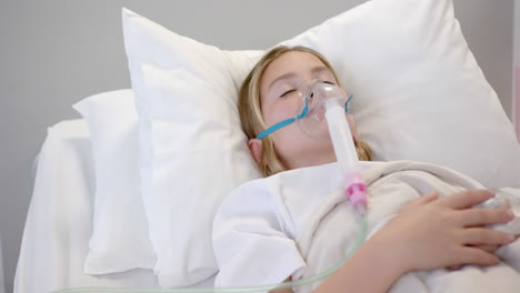 Caucasian-girl-patient-in-oxygen-mask-asleep-in-hospital-bed,-copy-space,-slow-motion