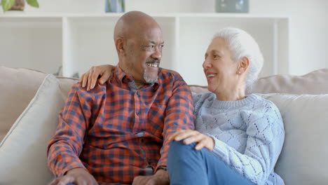 Portrait-of-happy-senior-biracial-couple-sitting-on-couch-embracing-and-talking-at-home,-slow-motion