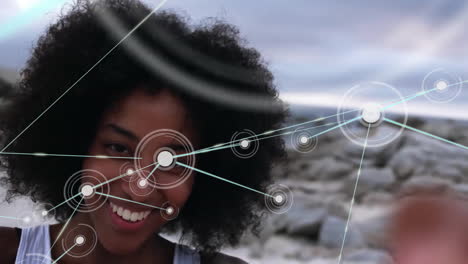 Animation-of-network-of-connections-with-icons-over-biracial-woman-by-sea