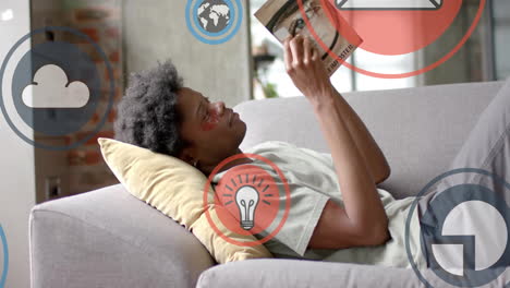 Animation-of-data-processing-over-african-american-man-reading-book-on-sofa