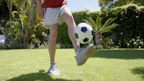 Low-section-of-biracial-man-juggling-football-with-feet-in-sunny-garden,-copy-space,-slow-motion
