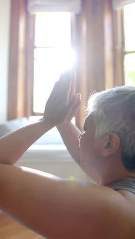 Video-Vertical-De-Una-Anciana-Birracial-Enfocada-Meditando-En-Casa,-Cámara-Lenta