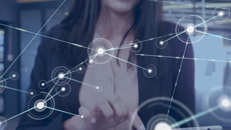 Animation-of-connected-dots-over-caucasian-businesswoman-standing-and-scrolling-on-digital-tablet